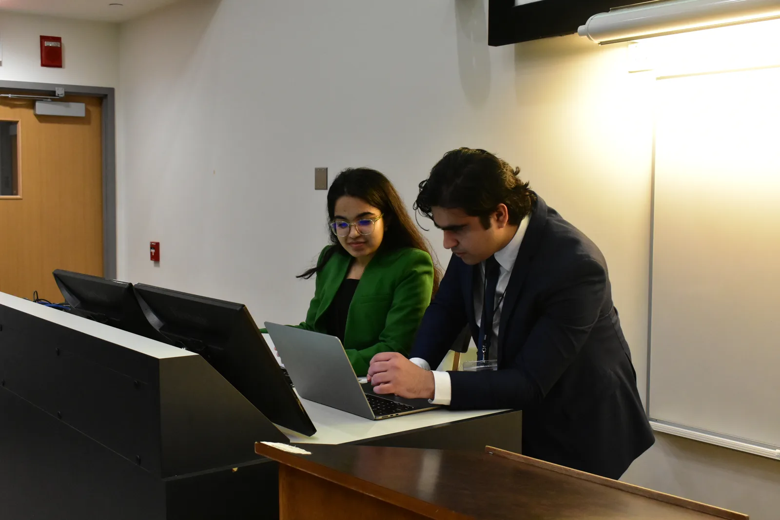 Two students in business dress working on a laptop at the podium during an ESA case competition